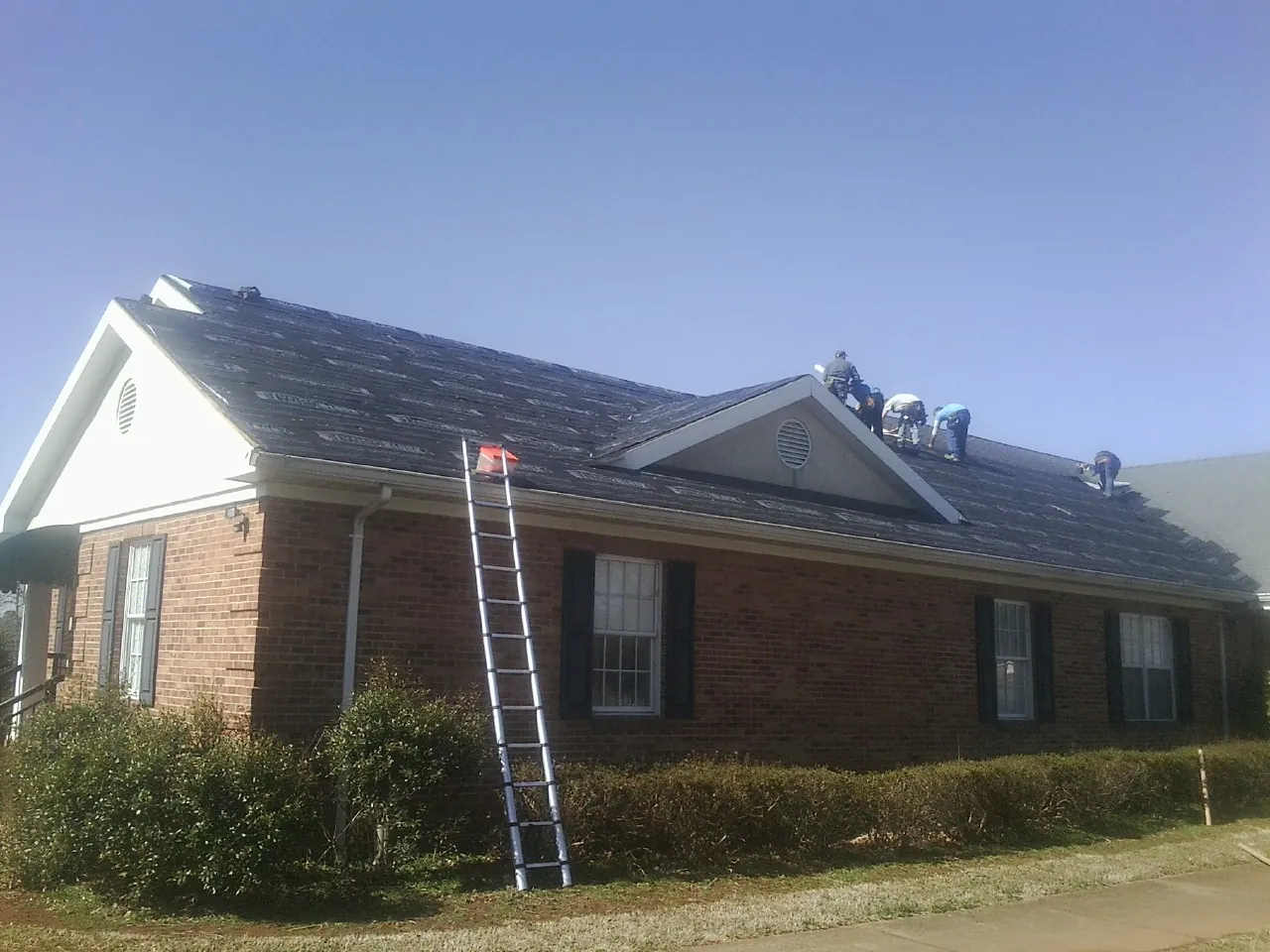 Crew tearing shingles off a brick ranch roof with a ladder set — Metal Roof Repair work by our crew in Hampshire