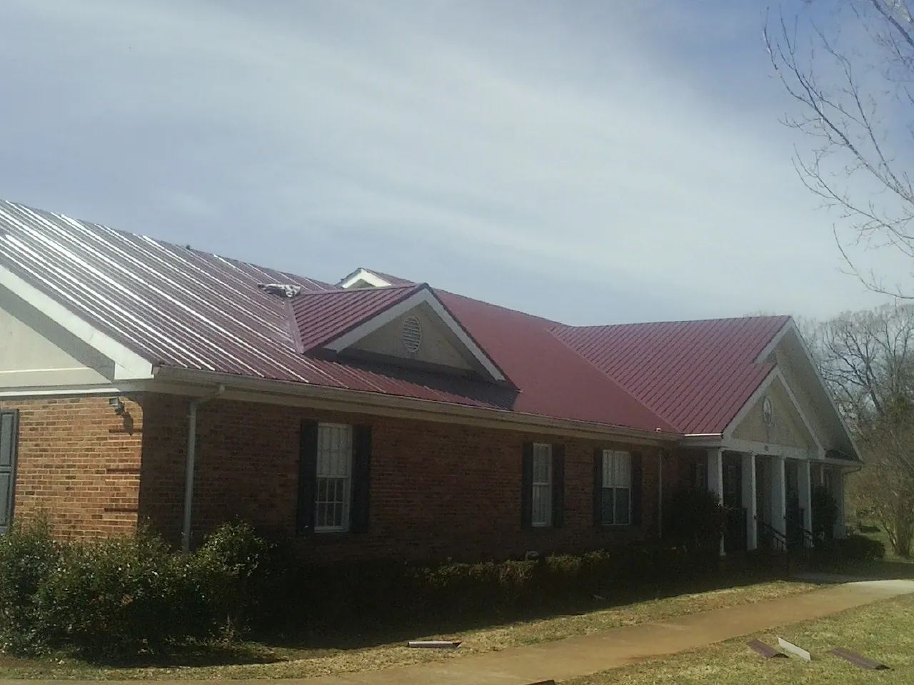 Red metal roof with gabled entries on a long brick building, from a Hail Damage Roof Repair job in Hampshire