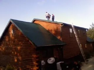 Crew on the ridge of a green metal roof on a two story log home in Hampshire