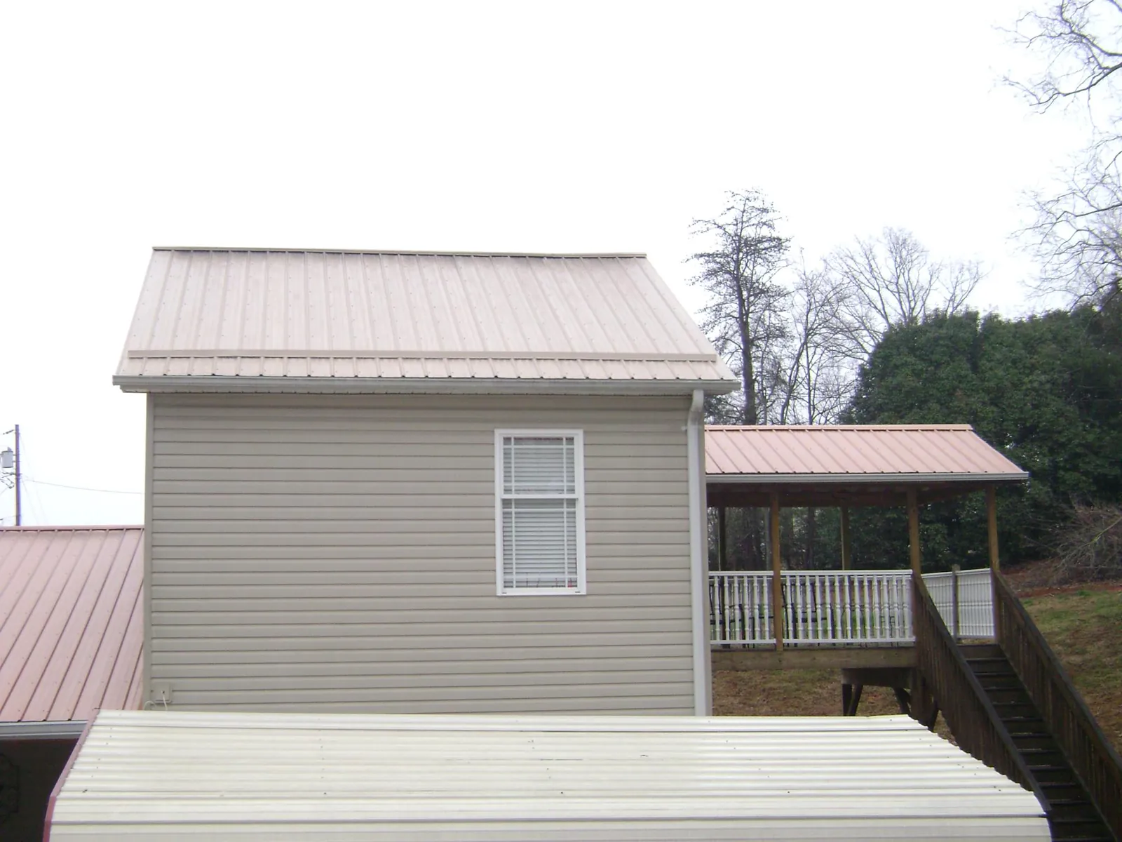 Tan metal roofs on a two story addition and attached porch, from a Roof Replacement job in Hampshire